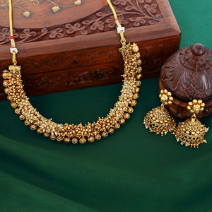 Gold necklace and earrings on a green surface with a wooden box in the background