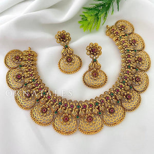 Matte gold South Indian choker with blossom-inspired motifs, ruby and green stones, filigree detailing, golden bead edging, and matching earrings.