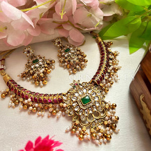 Matte gold South Indian choker necklace with emerald green rectangular stone, red and white kundan accents, pearl drops, and matching chandbali earrings.