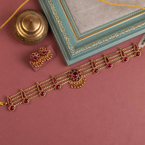 Traditional ruby kundan choker with crescent pendant, pearl drops, antique gold finish, and matching earrings.