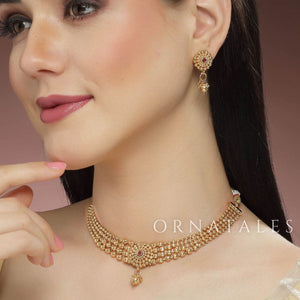 Rudrakshika temple choker necklace with triple golden bead layers, ruby lotus motif centerpiece, and miniature drop pendant detailing.