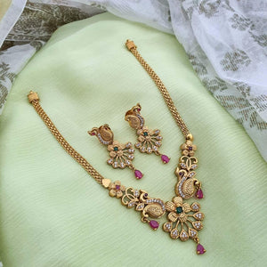 Temple-inspired peacock motif necklace with ruby and emerald stones, teardrop pendant, pearl drops, and antique gold finish.