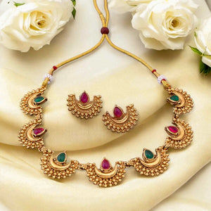 South Indian choker necklace with crescent motifs, red and green teardrop stones, antique matte gold finish, and matching half-moon earrings.
