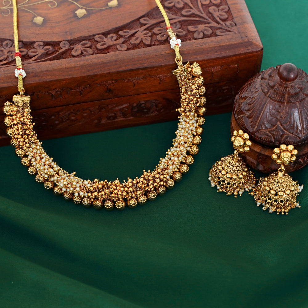 Gold necklace and earrings on a green surface with a wooden box in the background