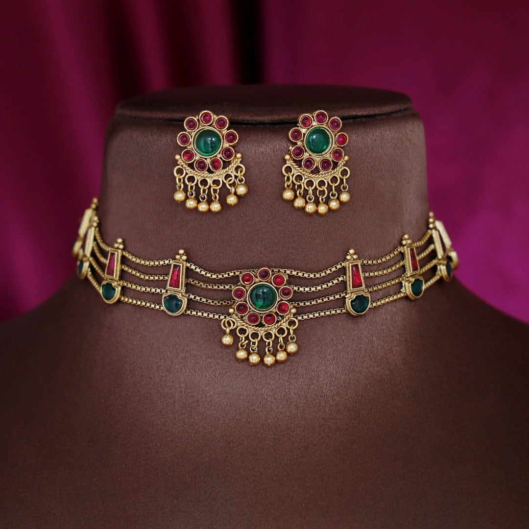 Traditional ruby emerald kundan choker with crescent pendant, pearl hangings, antique gold finish, and matching earrings.