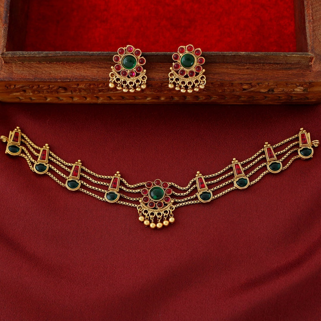 Traditional ruby emerald kundan choker with crescent pendant, pearl hangings, antique gold finish, and matching earrings.