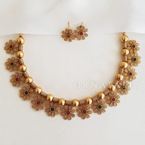 Floral motif choker necklace with ruby and emerald stones, gold base, ball-bead spacers, and matching stud earrings.