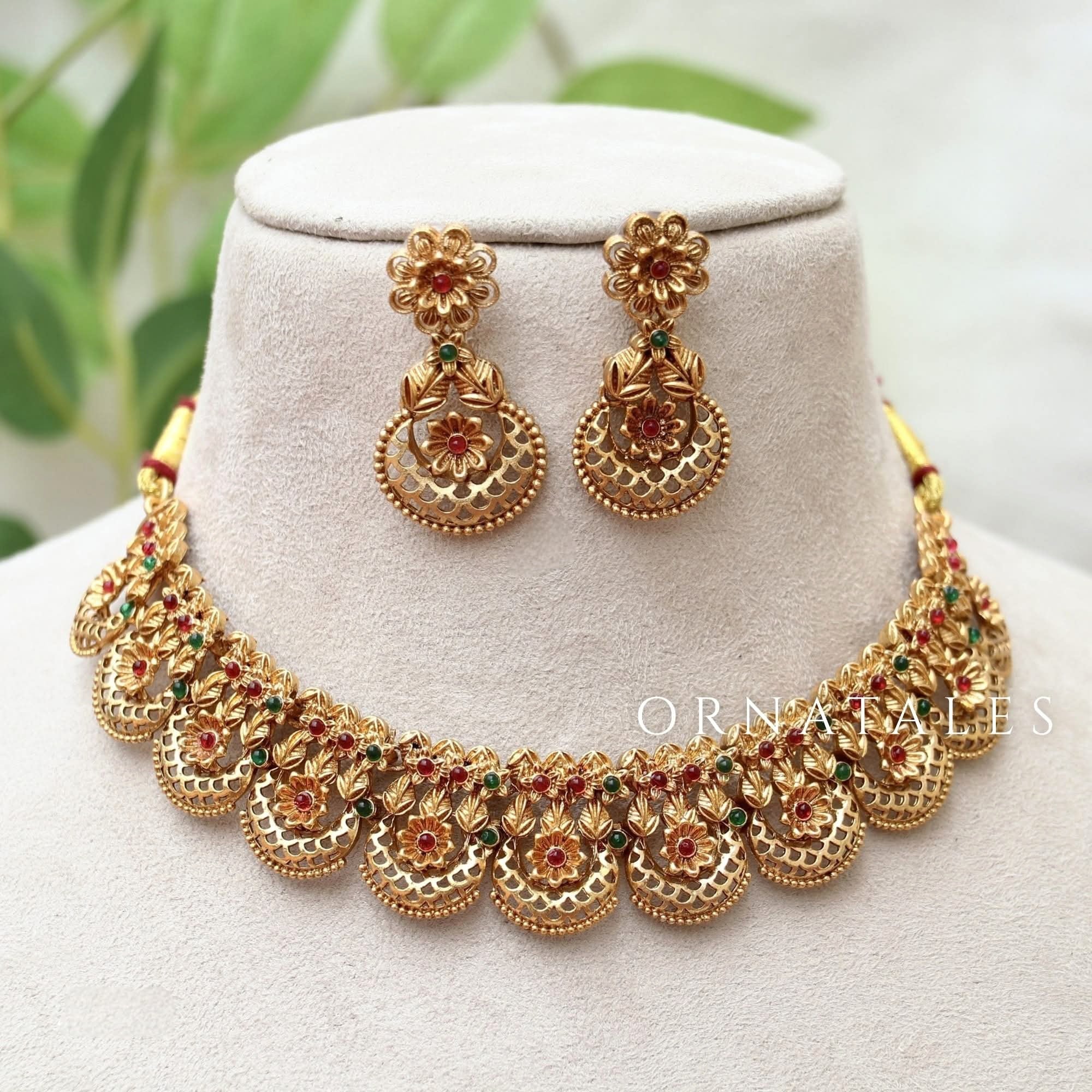 Matte gold South Indian choker necklace with circular floral carvings, red stone centers, white beaded edges, and matching floral drop earrings.