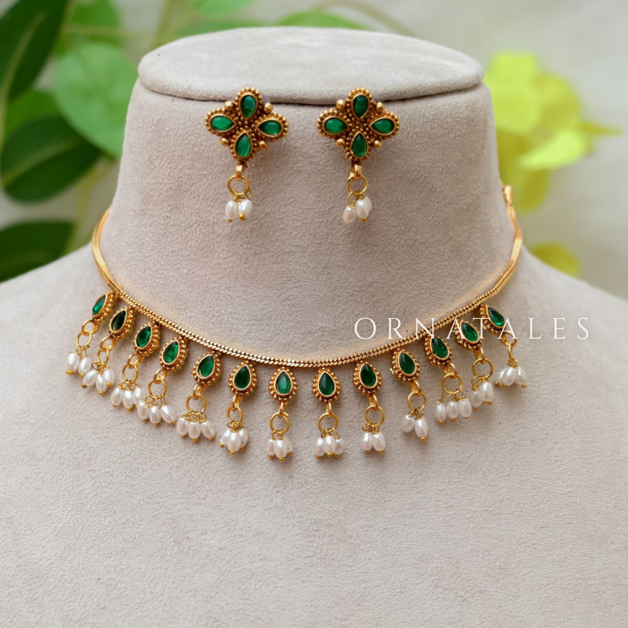 Matte gold South Indian choker with oval emerald green stones, pearl drop fringe, and matching floral earrings featuring pearl detailing.