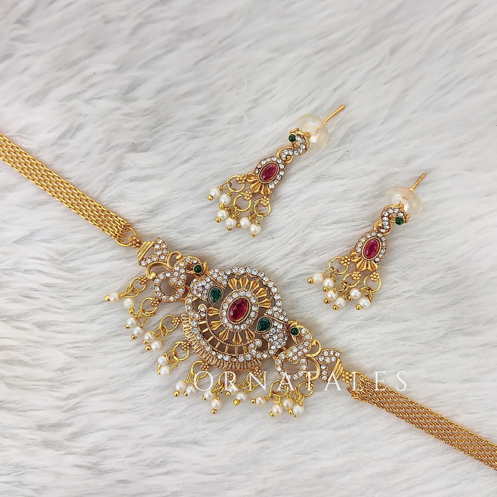 Matte gold South Indian choker with sunburst motif, red-green-white stones, pearl fringe, and matching elongated drop earrings.