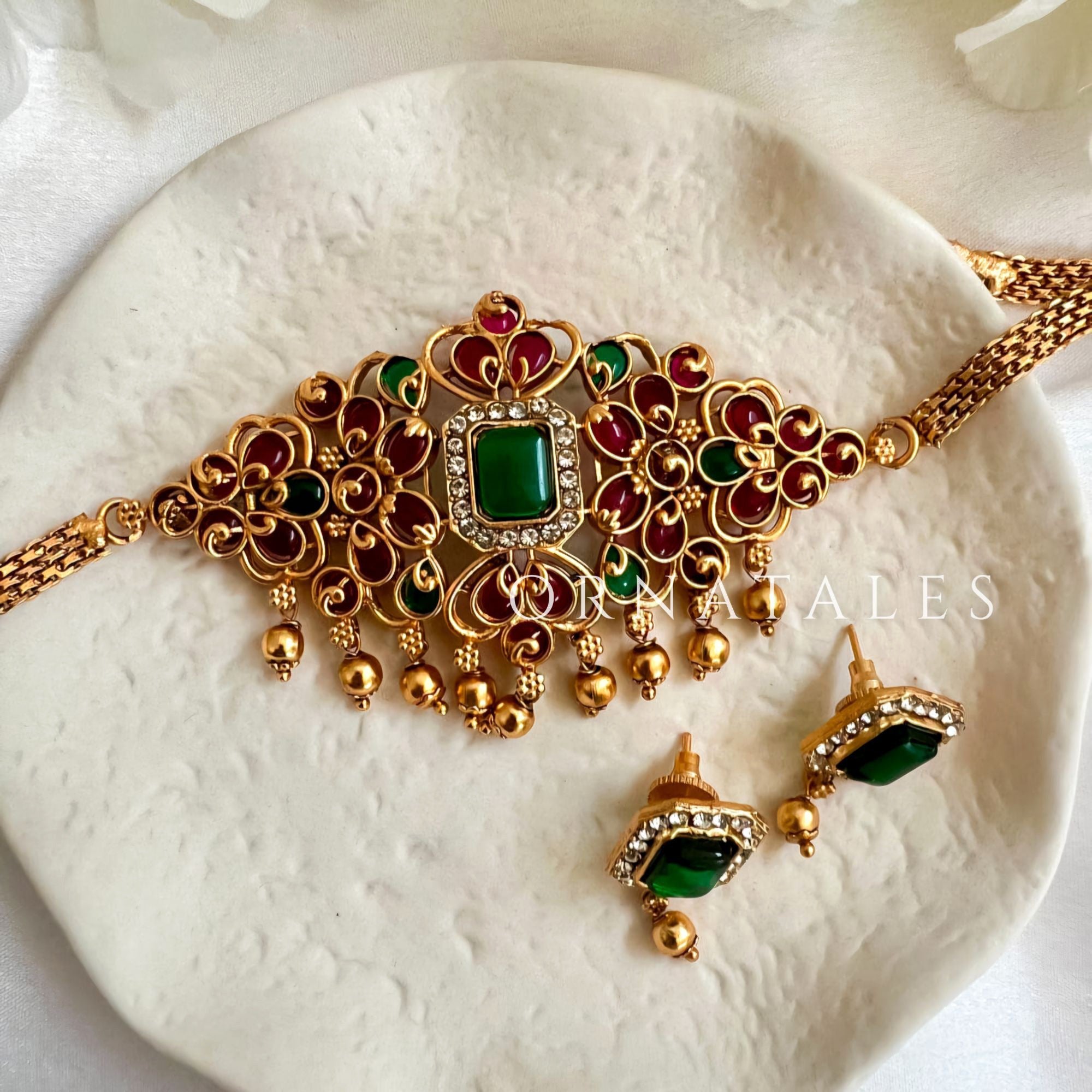 Matte gold South Indian choker with square emerald centerpiece, red & white enamel stones, filigree pattern, tiny gold drops, and matching rectangular emerald earrings.