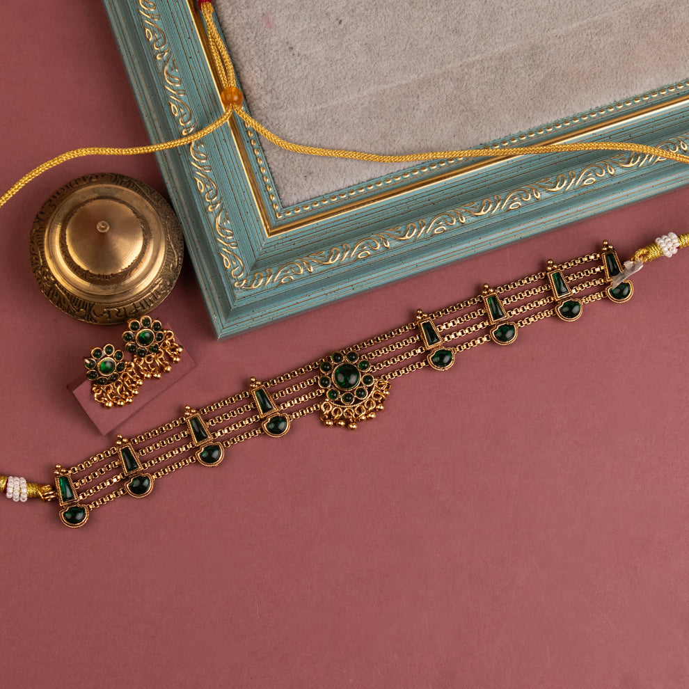 Traditional emerald kundan choker with crescent pendant, pearl hangings, antique gold finish, and matching earrings.