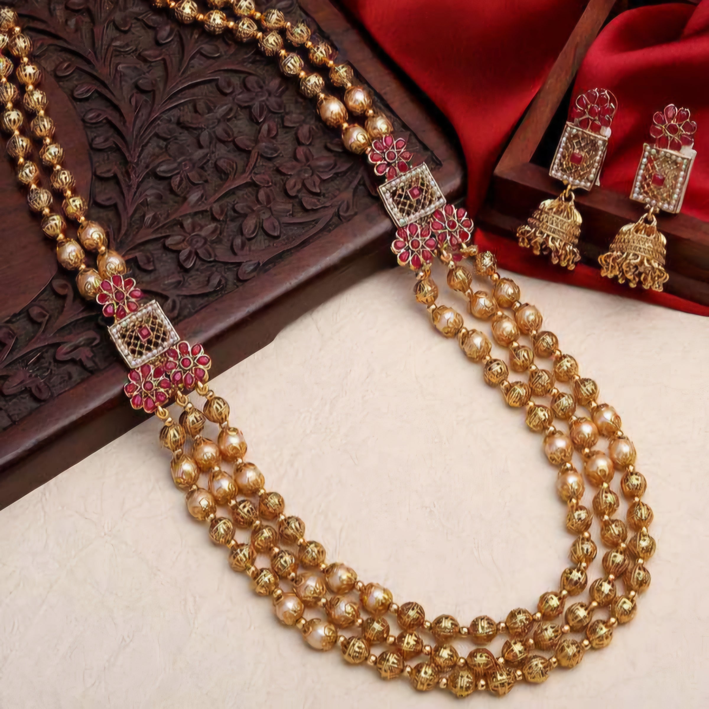 South Indian Sita necklace with three layers of matte gold beads, pearls, intricate beads, ruby flower motifs, square pendants, and matching earrings.