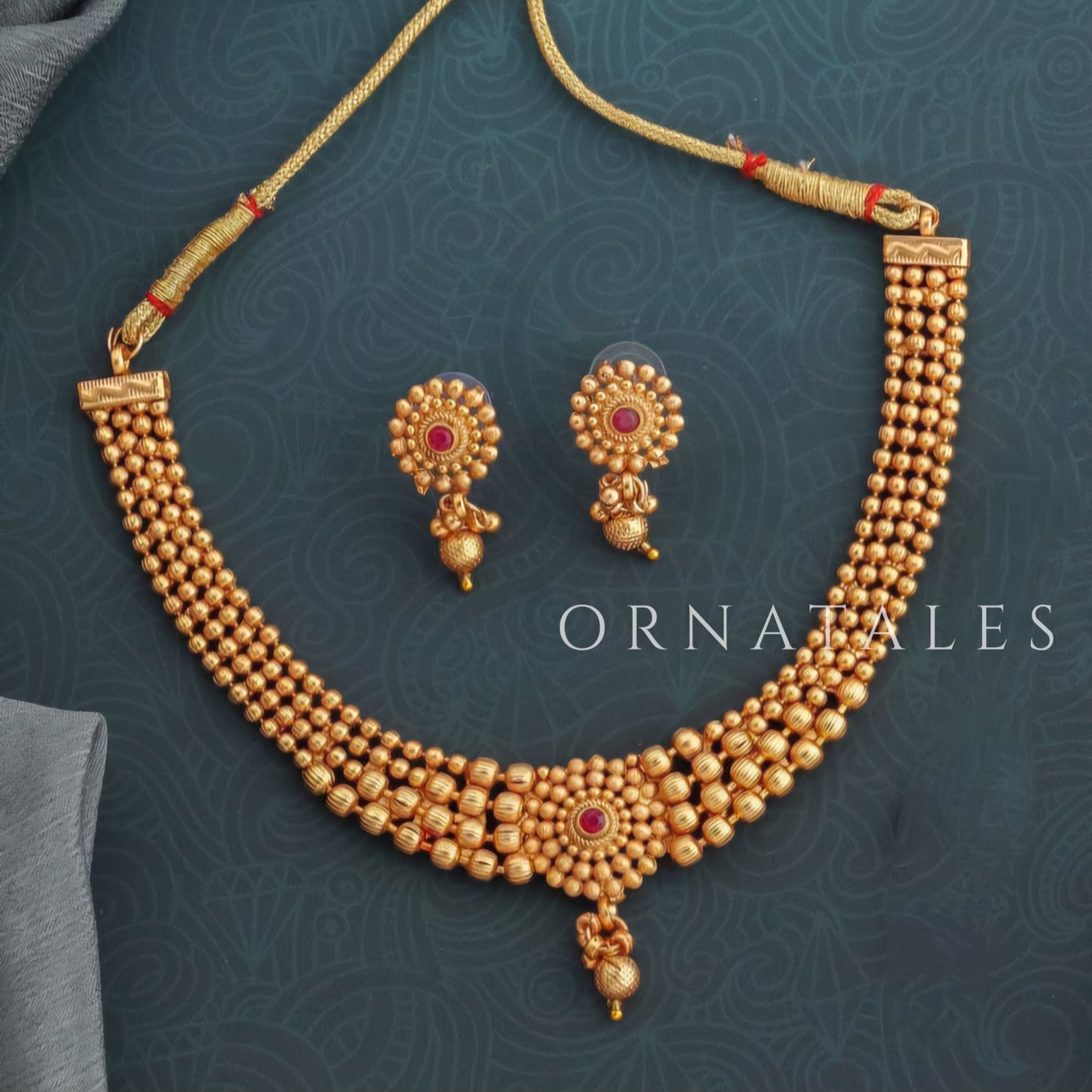 Rudrakshika temple choker necklace with triple golden bead layers, ruby lotus motif centerpiece, and miniature drop pendant detailing.