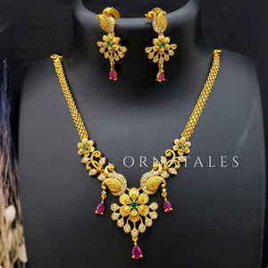 Temple-inspired peacock motif necklace with ruby and emerald stones, teardrop pendant, pearl drops, and antique gold finish.