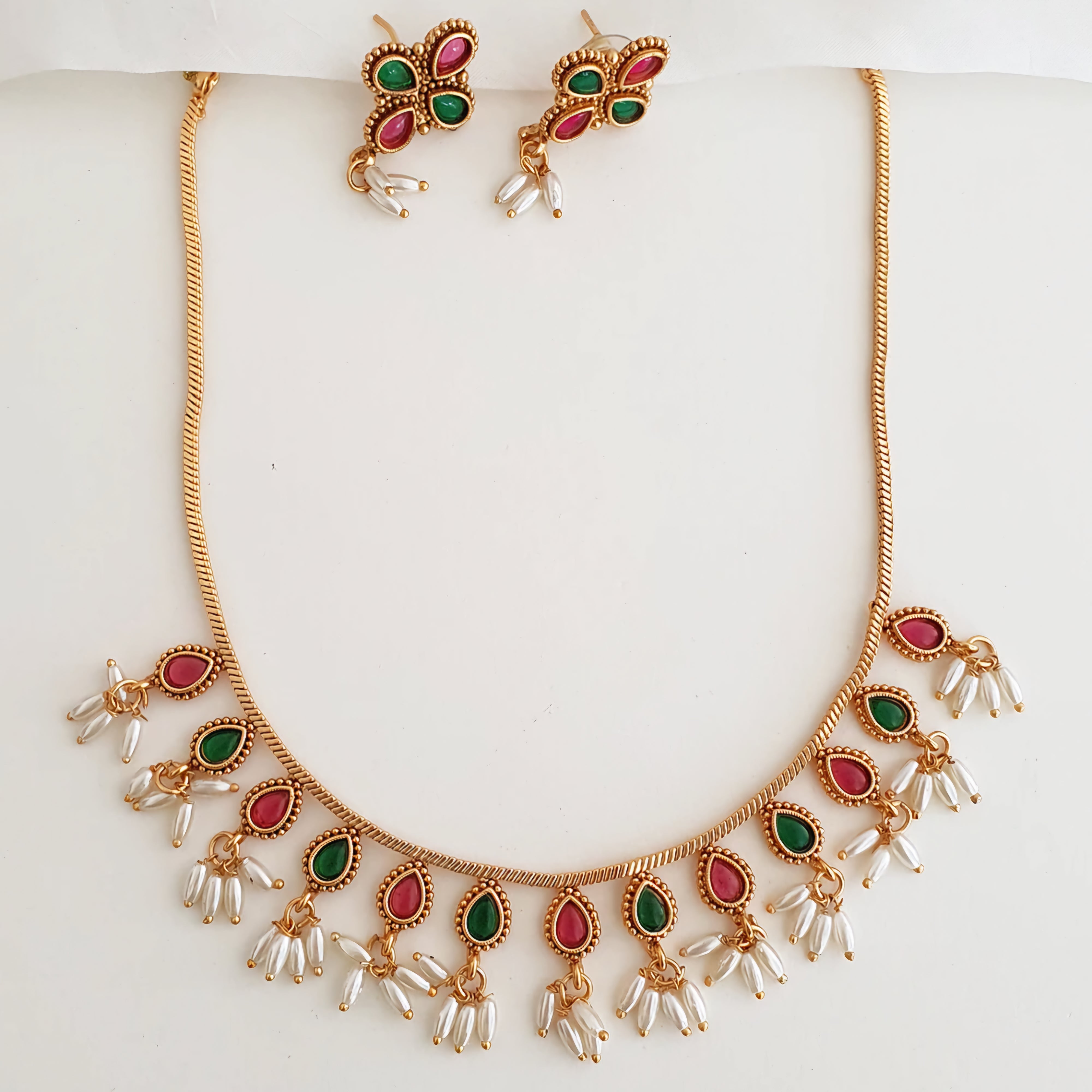 Matte gold South Indian choker with alternating emerald green and ruby stones, pearl drop fringe, and matching floral earrings.