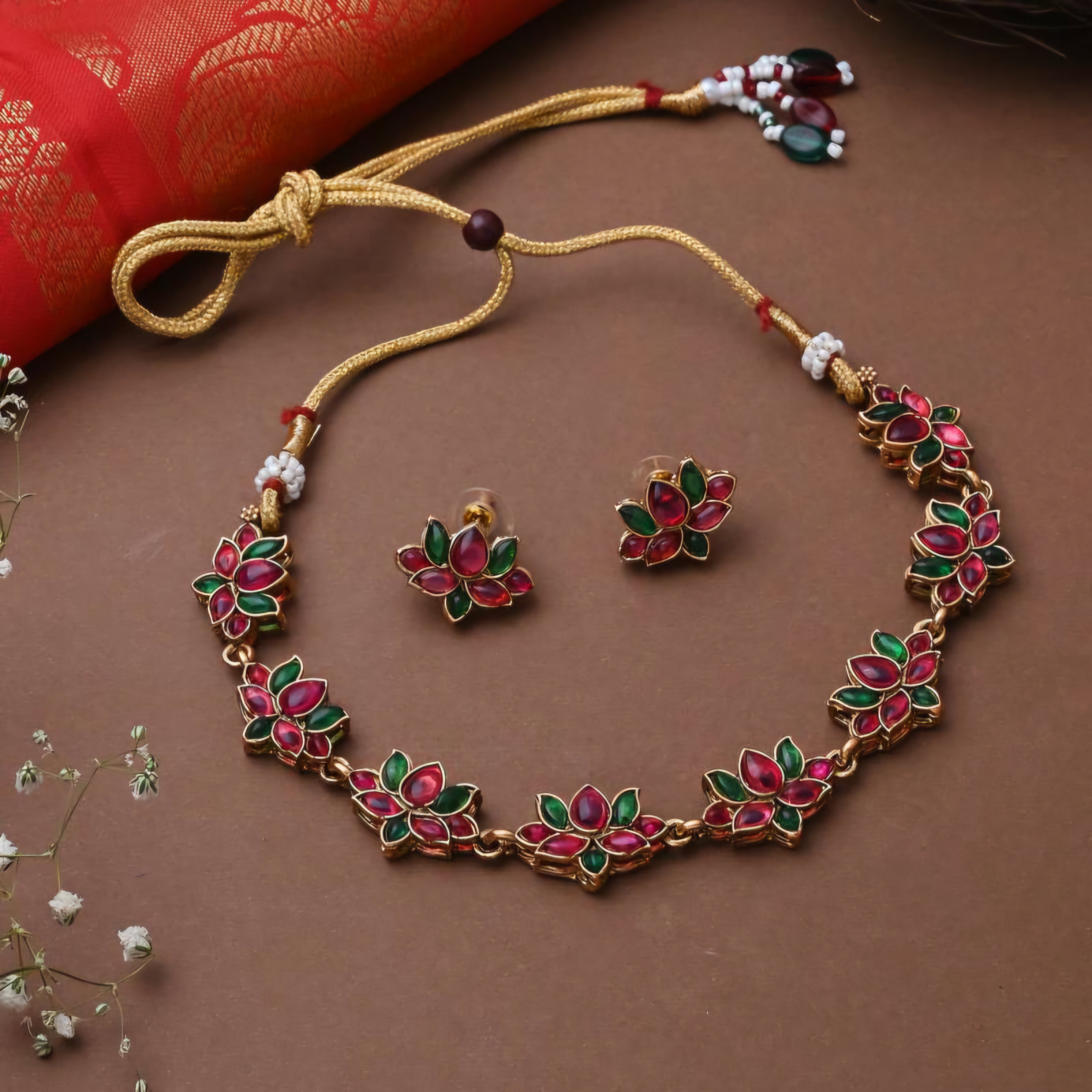 Matte gold South Indian choker with floral vine motifs, red and green enamel stones, flexible base, and matching floral stud earrings.