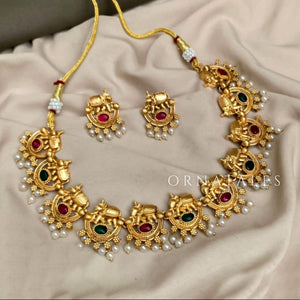 Matte gold South Indian choker with temple-style elephant (Hatimala) motifs, red and green stones, pearl fringe, and matching jhumka earrings.