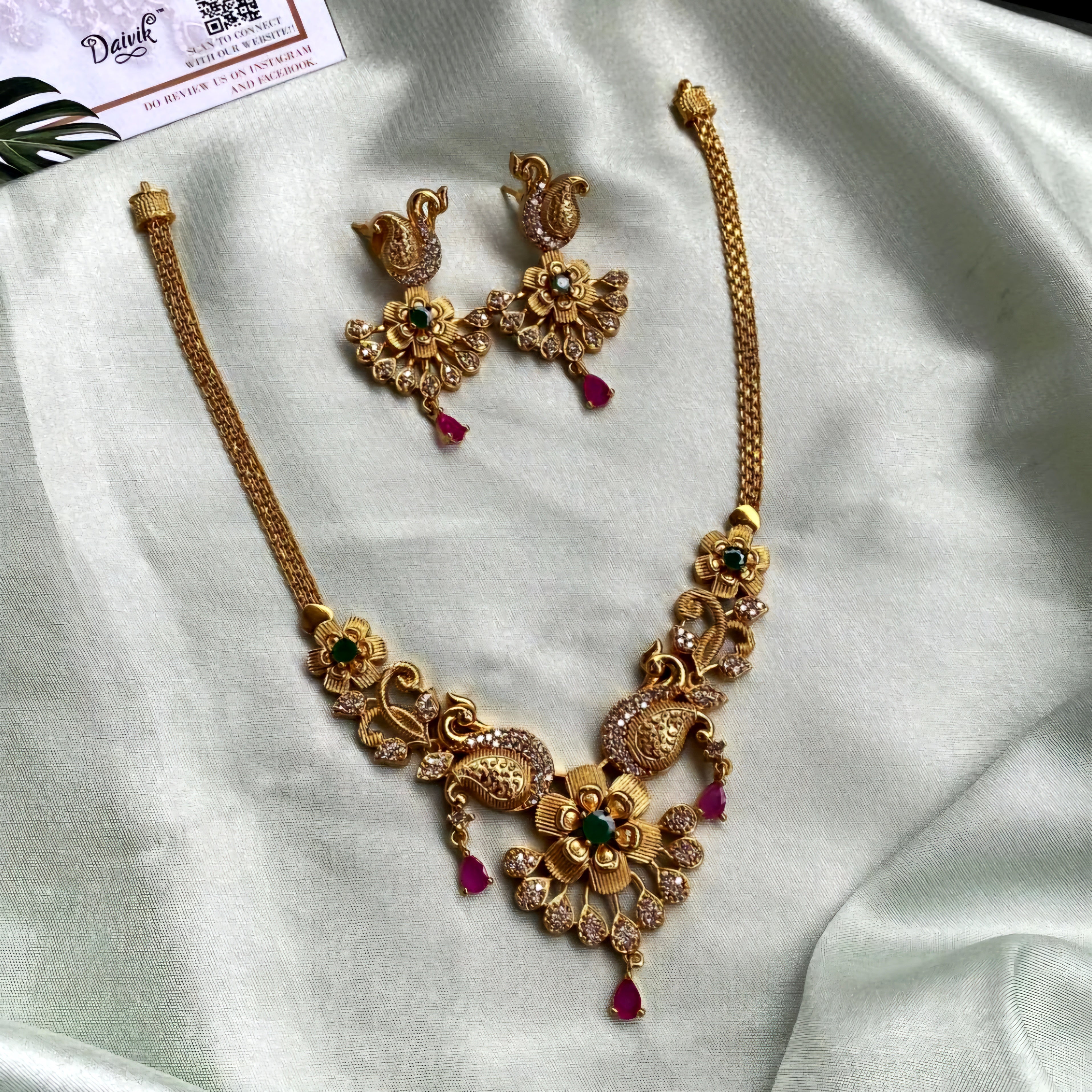 Temple-inspired peacock motif necklace with ruby and emerald stones, teardrop pendant, pearl drops, and antique gold finish.