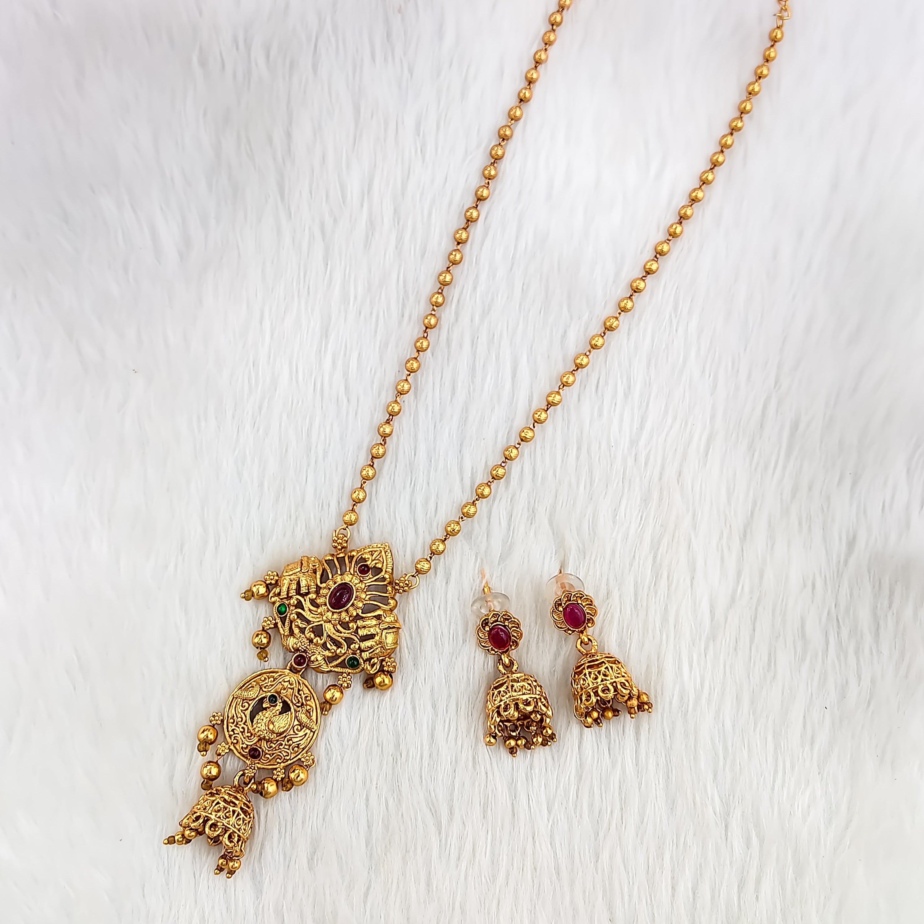 Traditional South Indian Sita necklace with peacock motif, floral embossed pendant, deep ruby stone, ghungroo beads, and matching jhumka earrings.