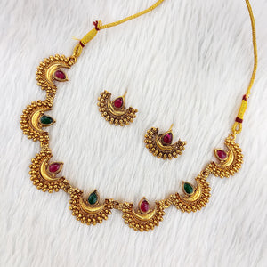 South Indian choker necklace with crescent motifs, red and green teardrop stones, antique matte gold finish, and matching half-moon earrings.