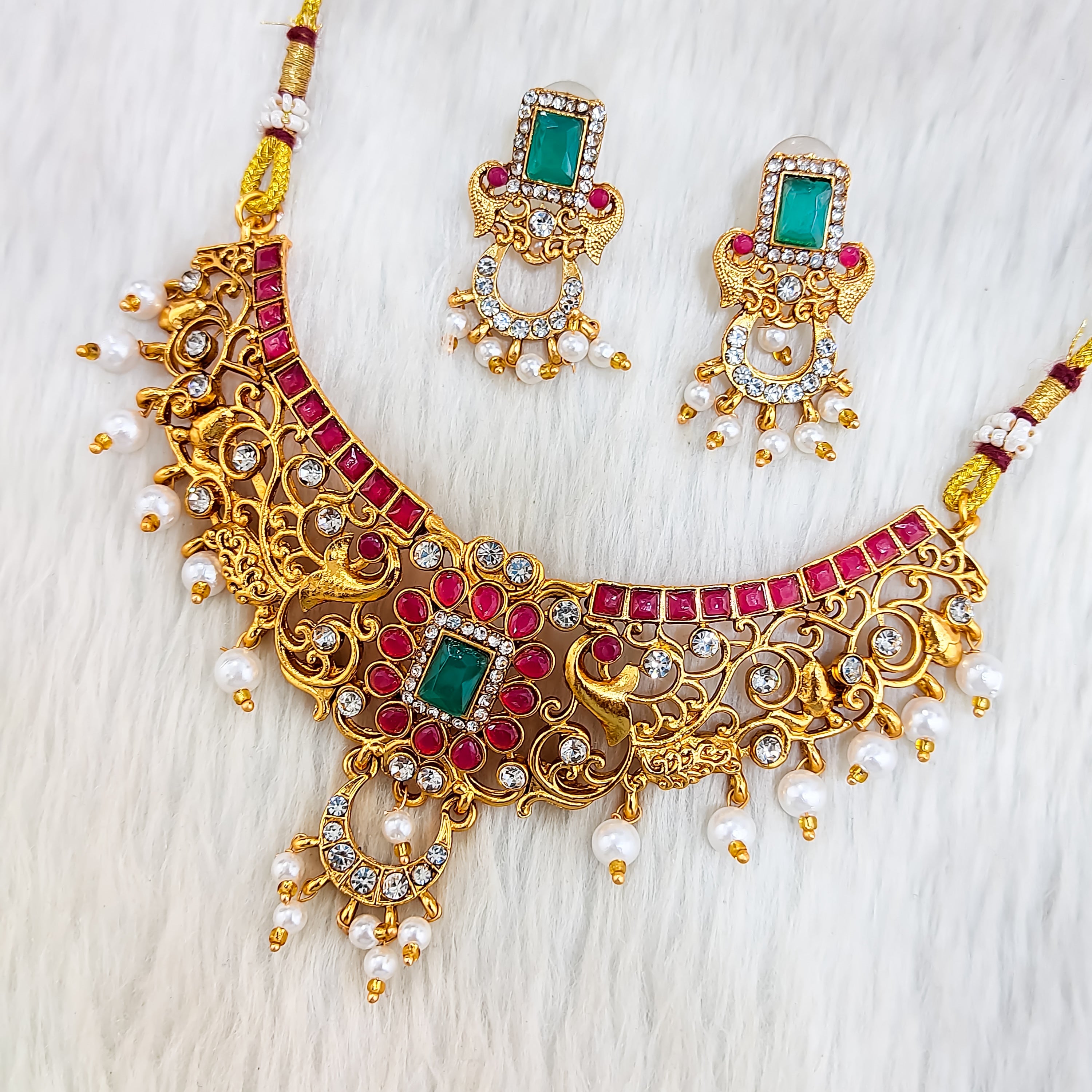South Indian choker necklace with square emerald centerpiece, red stones, white pearl drops, intricate filigree, matte gold finish, and matching rectangular earrings.