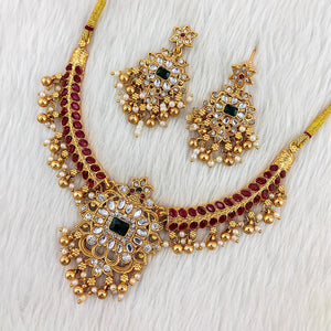 Matte gold South Indian choker necklace with emerald green rectangular stone, red and white kundan accents, pearl drops, and matching chandbali earrings.