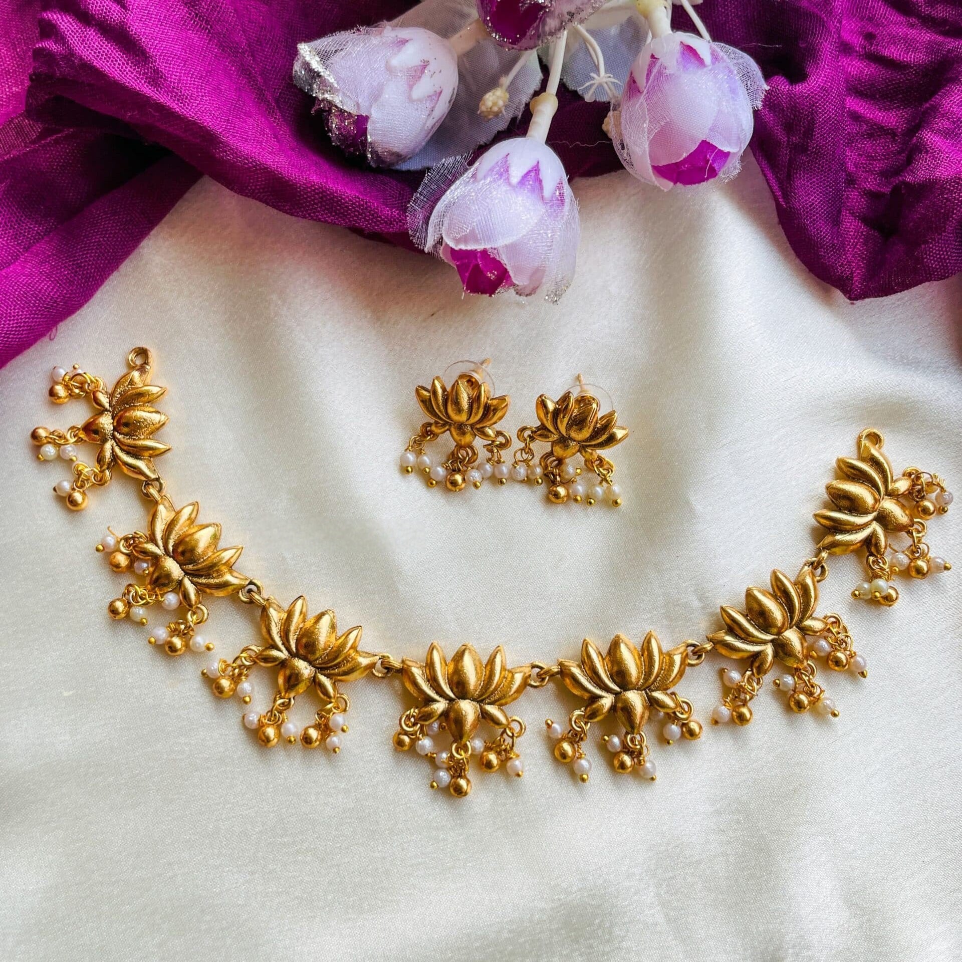 Suvarna Padmakshi Necklace Set with matte gold lotus motifs, dangling pearl details, and matching earrings in traditional temple-inspired design.