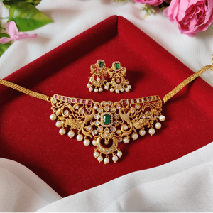 South Indian choker necklace with square emerald centerpiece, red stones, white pearl drops, intricate filigree, matte gold finish, and matching rectangular earrings.