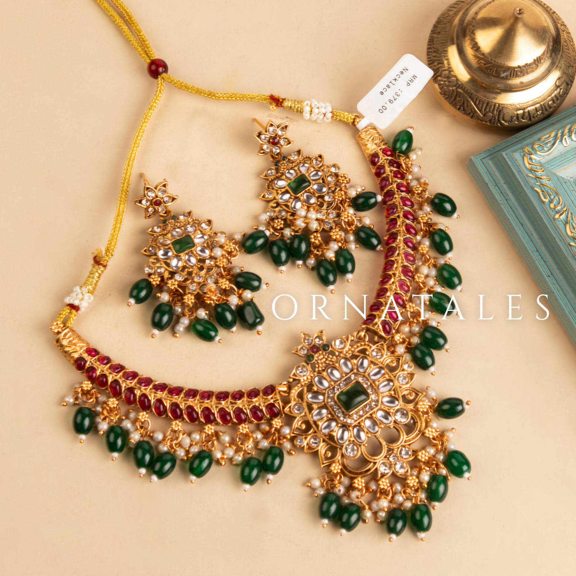 Temple-inspired Emerald Kumuda necklace set featuring green teardrop stones, red kundans, and a center emerald-cut stone.